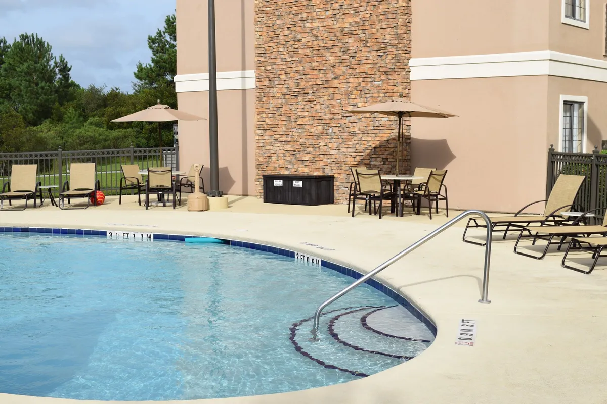 This vibrant exterior image features a spacious swimming pool bordered by a natural stone wall. Lounge chairs and umbrellas are scattered around the pool, providing comfortable spots for sunbathing, relaxing, or socializing. The setting suggests a welcoming environment for both active and leisurely pursuits, and the golden-hour lighting evokes a sense of relaxation and luxury.