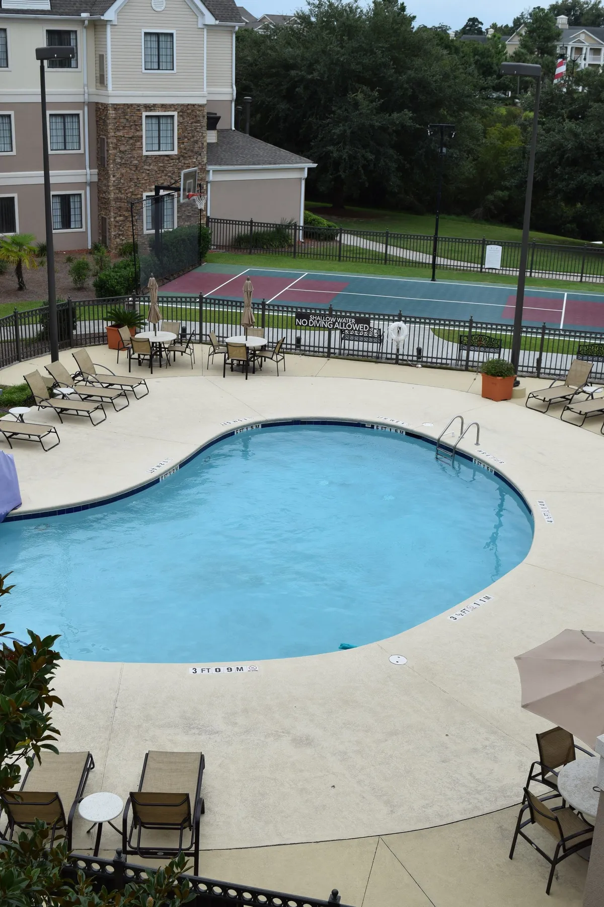 This exterior shot encompasses a sparkling swimming pool with lounge chairs and an adjacent tennis court, offering space for both relaxation and active recreation under the sun.