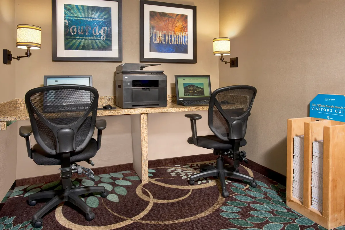This interior image captures a business center setup with a computer station, printer, wall artwork, and a visitor's guide display, all arranged to foster productivity and efficiency.