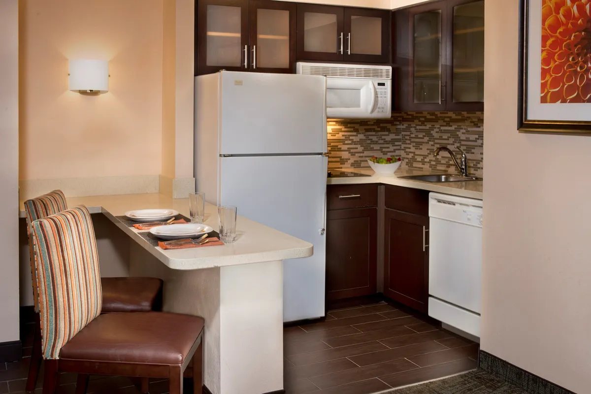 A modern kitchen area with a central island, stainless steel refrigerator, dishwasher, and a colorful tile backsplash. The space is open and inviting, ideal for preparing meals or gathering for a casual coffee.