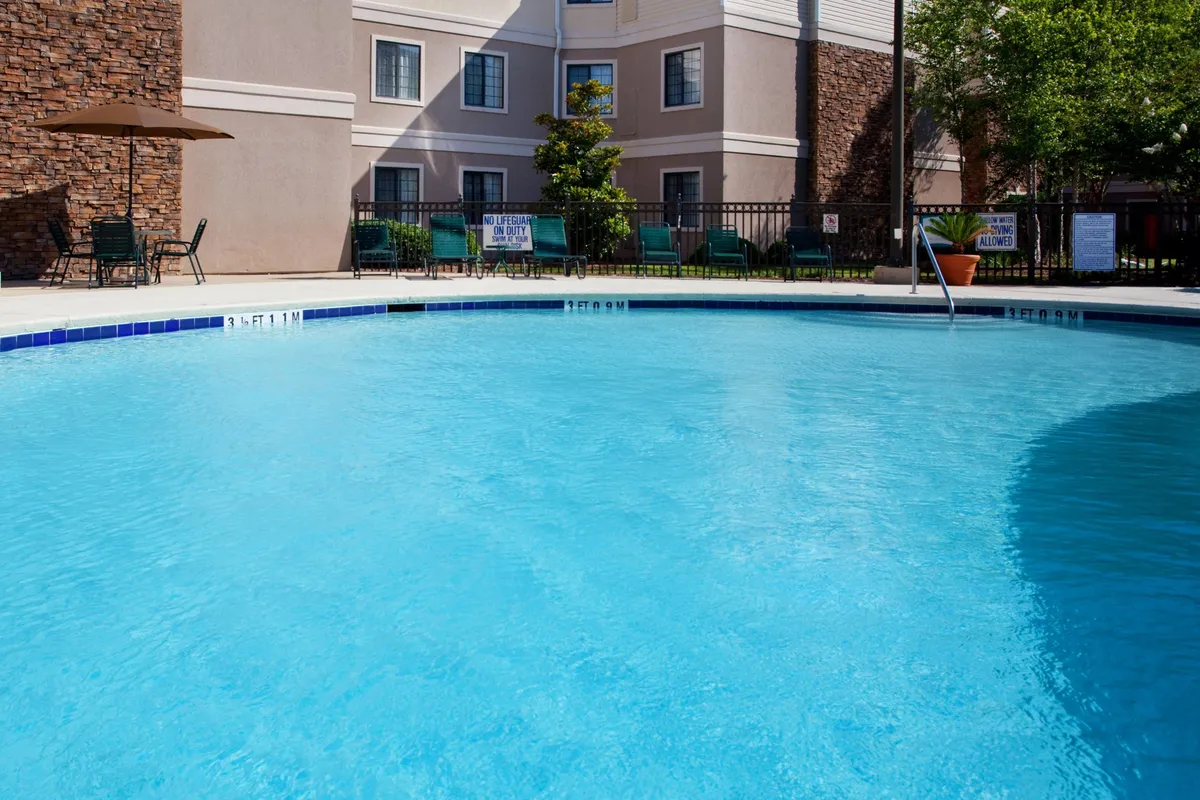 This inviting exterior image showcases the property’s sparkling swimming pool, surrounded by comfortable lounge chairs and umbrellas. The building facade is prominently featured in the background, offering a sense of the property’s welcoming atmosphere and convenient amenities. The scene is bathed in warm, natural light, hinting at both relaxation and productive social gatherings.