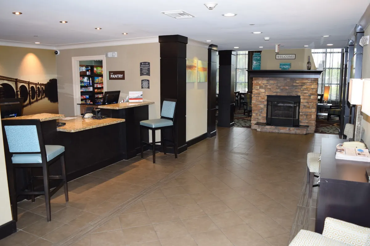 A cozy indoor common area featuring a reception desk, fireplace, comfortable seating, and a food pantry. The warm lighting and inviting furnishings create a sense of welcome and comfort.