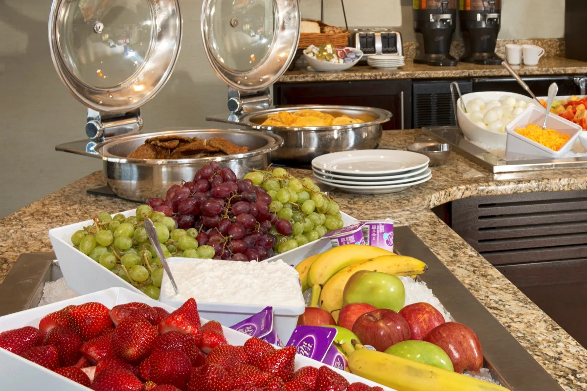 A cheerful breakfast area featuring a spread of fresh fruits, breakfast items, and modern coffee machines. Guests are seen enjoying breakfast, chatting, and prepping for their day in a bright, welcoming space.