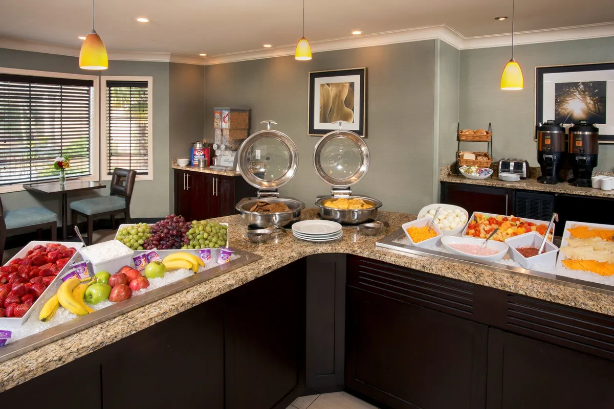 This image features a buffet table laden with an assortment of breakfast items, a seating area for guests, and a coffee station. The atmosphere is bright and welcoming, suggesting a pleasant communal dining experience.